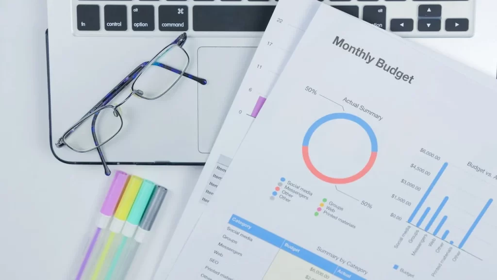 A clean office desk setup featuring a laptop, glasses, and a colorful budget report.